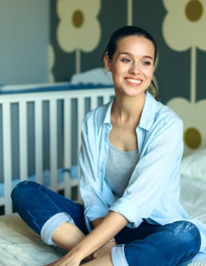 Yatakta çocuk karyolası yakın oturan genç kadın.