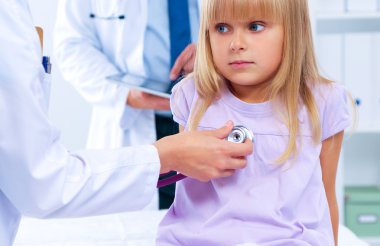 Kadın doktor ameliyatta steteskopla çocuğu muayene ediyor.