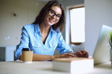 Ofis masasında dizüstü bilgisayarıyla oturan genç bir kadın.