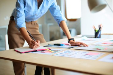 Enstrümanlar, planlar ve dizüstü bilgisayarlarla masanın yanında duran genç bir kadın.