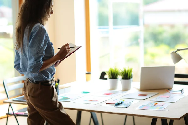 Young woman standing near desk with instruments, plan and laptop — Stock Photo, Image