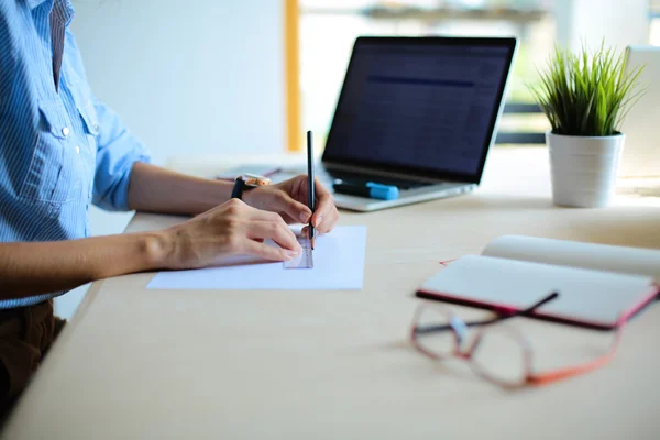 Young woman sitting at the desk with instruments, plan and laptop — Stock Photo, Image