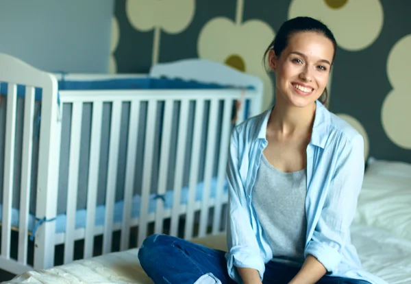 Mujer joven sentada en la cama cerca de cuna de los niños . — Foto de Stock