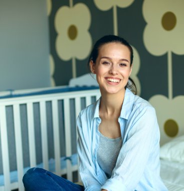 Yatakta çocuk karyolası yakın oturan genç kadın.