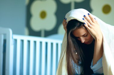 Yatakta çocuk karyolası yakın oturan genç yorgun kadın.