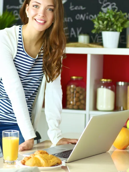 Mujer joven sentada cerca de escritorio en la cocina —  Fotos de Stock