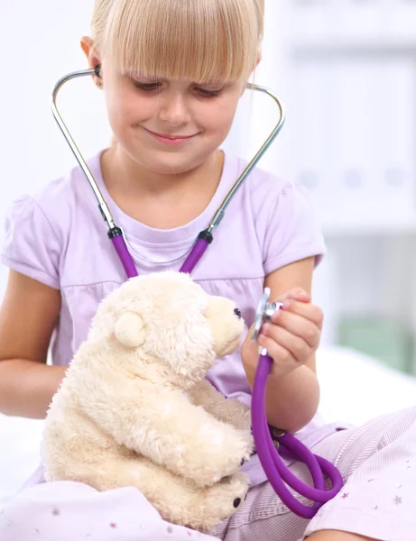 小女孩正在用听诊器检查她的玩具熊 免版税图库照片