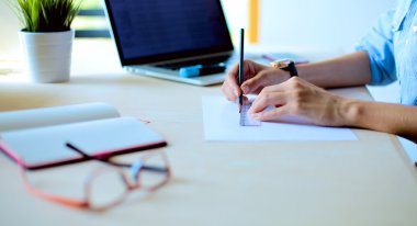 Masasında enstrümanlar, planlar ve dizüstü bilgisayarlarla oturan genç bir kadın.