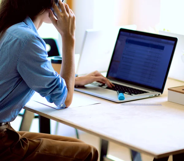 Beautiful young business woman sitting at office desk and talking on cell phone