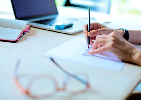 Jeune femme assise au bureau avec instruments, plan et ordinateur portable — Photo