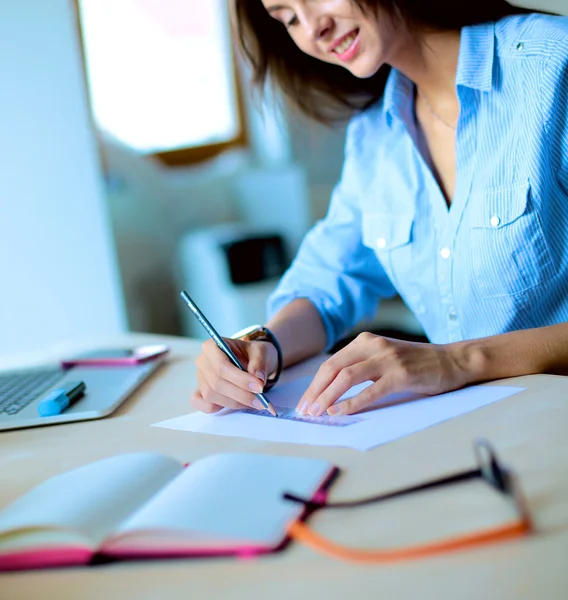 Jonge vrouw zit aan het bureau met instrumenten, plan en laptop — Stockfoto