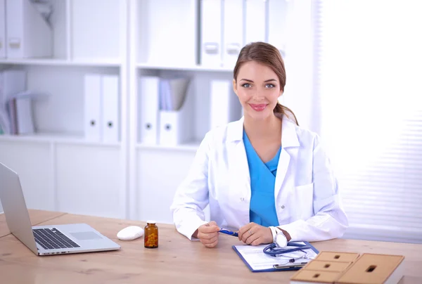 Belle jeune femme médecin souriante assise au bureau et écrivant. — Photo