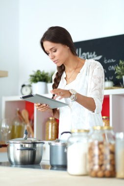Mutfakta yemek yapmak için tablet bilgisayar kullanan genç bir kadın. .