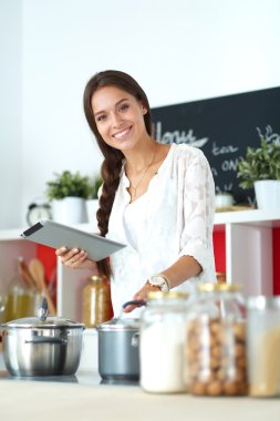 Mutfakta yemek yapmak için tablet bilgisayar kullanan genç bir kadın. .