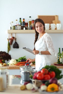 Mutfakta yemek yapmak için tablet bilgisayar kullanan genç bir kadın. .