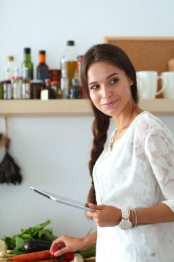 Mutfakta yemek yapmak için tablet bilgisayar kullanan genç bir kadın. .