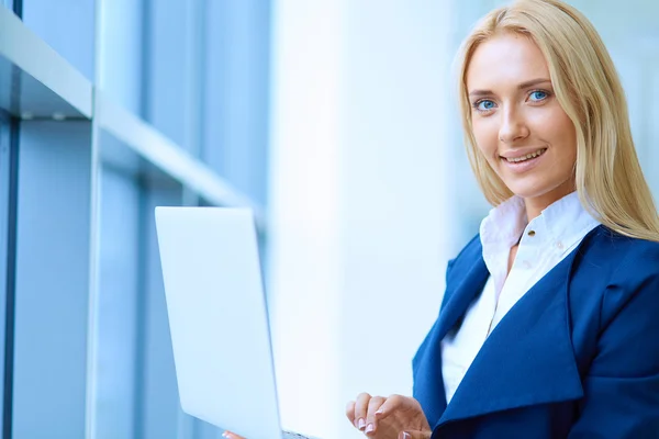 Businesswoman standing against office window holding laptop — Stock Photo, Image