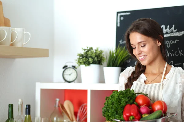 Glimlachende jonge vrouw met groenten in de keuken — Stockfoto