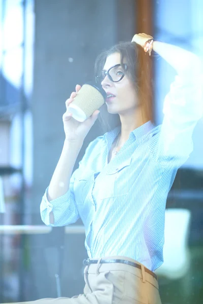 Empresaria bebiendo de la taza mientras trabaja en el portátil en la oficina —  Fotos de Stock