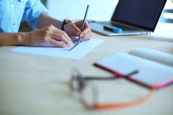 Jeune femme assise au bureau avec instruments, plan et ordinateur portable — Photo