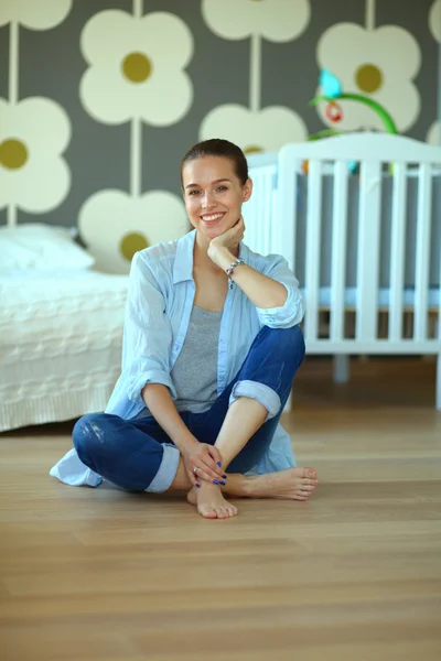 Young woman sitting on the floor near childrens cot. — Stock Photo, Image