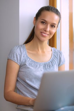 Genç ve güzel bir kadın evde dizüstü bilgisayar kullanıyor.