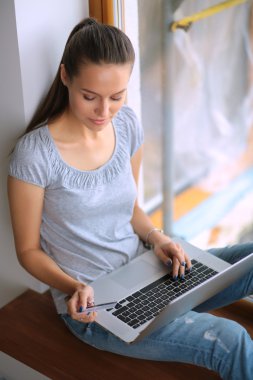 Genç ve güzel bir kadın evde dizüstü bilgisayar kullanıyor.