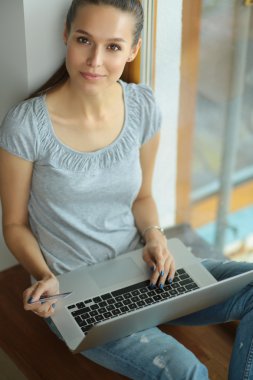 Genç ve güzel bir kadın evde dizüstü bilgisayar kullanıyor.