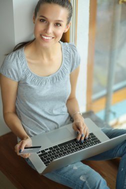 Genç ve güzel bir kadın evde dizüstü bilgisayar kullanıyor.