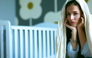 Yatakta çocuk karyolası yakın oturan genç yorgun kadın.