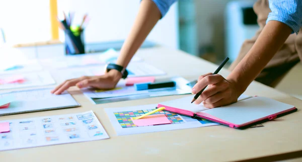 Jeune femme debout près du bureau avec des instruments, plan et ordinateur portable — Photo