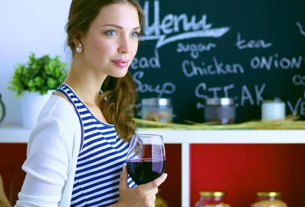 Mujer bonita bebiendo un poco de vino en casa en la cocina . —  Fotos de Stock