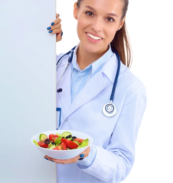 Retrato de una hermosa doctora sosteniendo un plato con verduras frescas en blanco — Foto de Stock