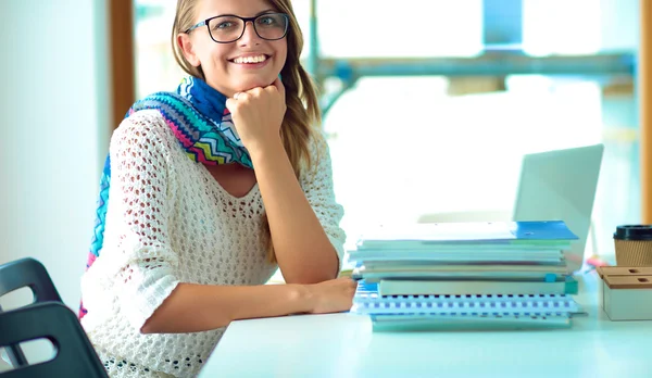 Jeune femme assise à un bureau parmi les livres — Photo