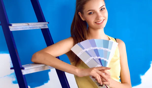 Jovem bela mulher segurando paleta de cores, de pé perto da parede . — Fotografia de Stock