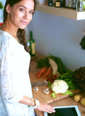 Mutfakta yemek yapmak için tablet bilgisayar kullanan genç bir kadın.