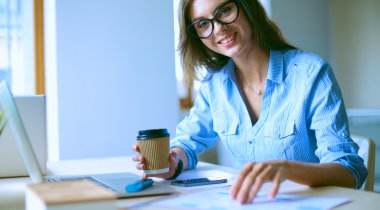 Ofis masasında dizüstü bilgisayarıyla oturan genç bir kadın.