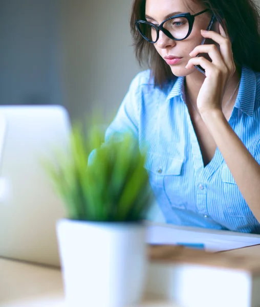 Mooie jonge zakenvrouw zitten aan het bureau en praten op mobiele telefoon — Stockfoto