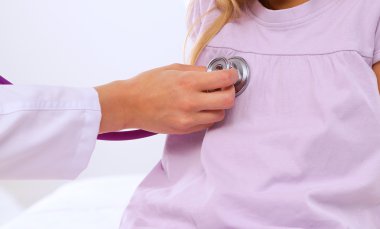 Kadın doktor ameliyatta steteskopla çocuğu muayene ediyor.