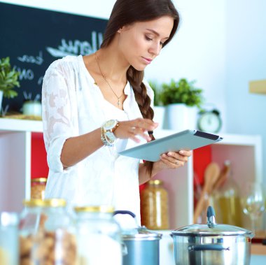 Mutfakta yemek yapmak için tablet bilgisayar kullanan genç bir kadın. .