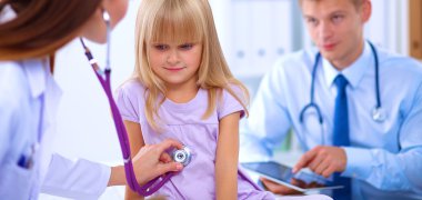 Kadın doktor ameliyatta steteskopla çocuğu muayene ediyor.