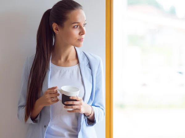 Atractiva mujer sentada en el escritorio en la oficina tomando café para llevar . —  Fotos de Stock