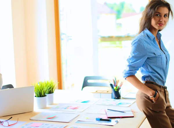 Jonge vrouw in de buurt van bureau met instrumenten, plan en laptop — Stockfoto