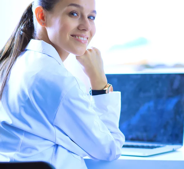 Hermosa joven sonriente doctora sentada en el escritorio —  Fotos de Stock