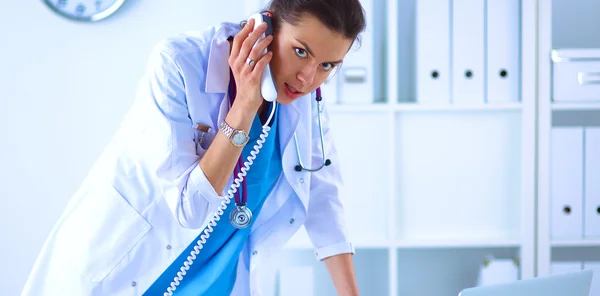 Jovem médico mulher em casaco branco no computador usando telefone — Fotografia de Stock