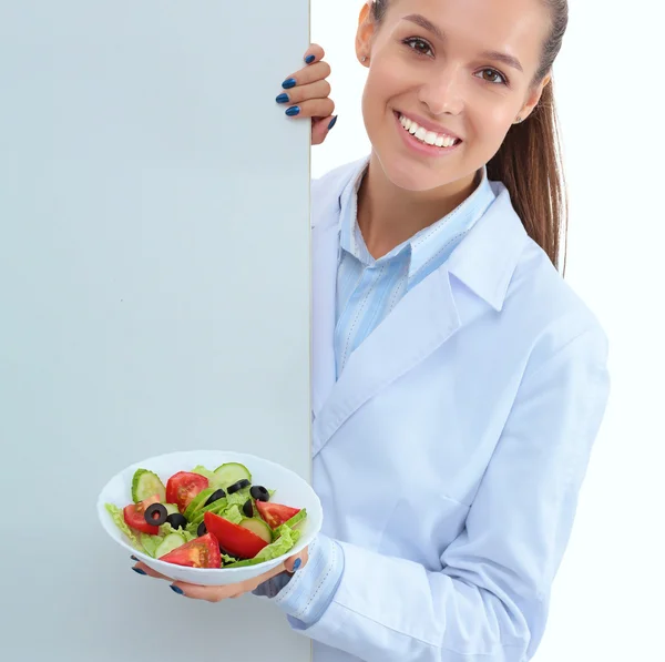 Retrato de una hermosa doctora sosteniendo un plato con verduras frescas en blanco — Foto de Stock