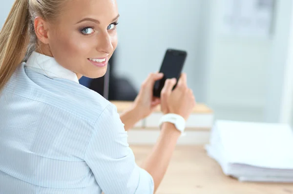 Businesswoman sending message with smartphone sitting in the office — Stock Photo, Image