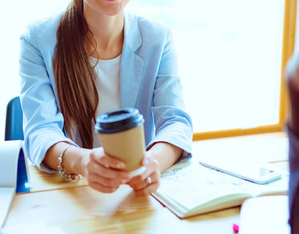 Aantrekkelijke vrouw achter balie in kantoor, werken met de laptop, afhaalmaaltijden kop koffie. — Stockfoto