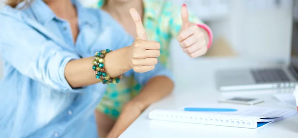 Due donne che lavorano insieme in ufficio, sedute sulla scrivania e mostrando ok — Foto Stock