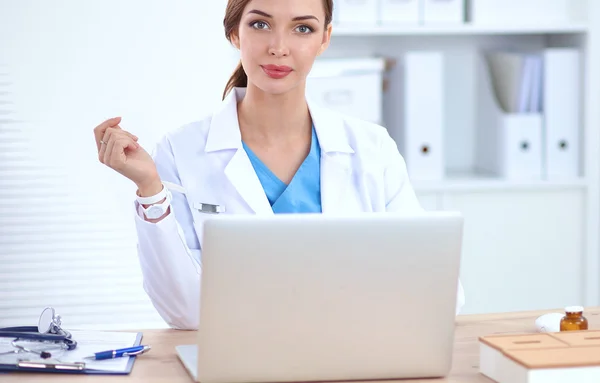 Schöne junge lächelnde Ärztin sitzt am Schreibtisch und schreibt. — Stockfoto